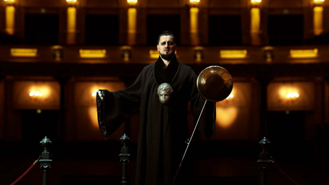Konstantyn Napolov steht in einem dunkel beleuchteten Theater mit einem schwarzen Gewand